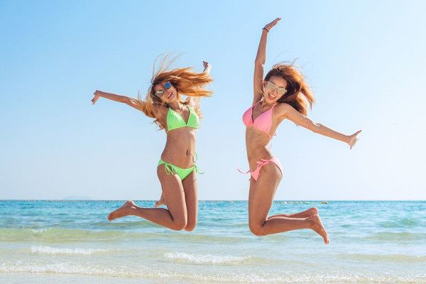 Happy bikini two asian women jumping of joy and success on perfect white sand beach on italian vacation. Holiday girls with sexy slim suntan body running of freedom and happiness.