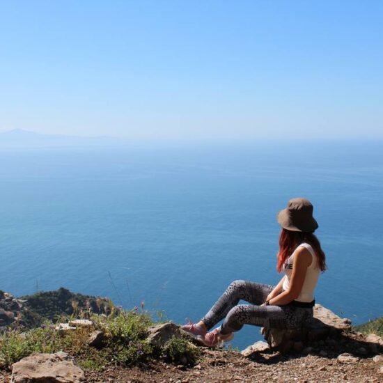 Ragazza escursionista seduta su una roccia che fissa l'orizzonte.
