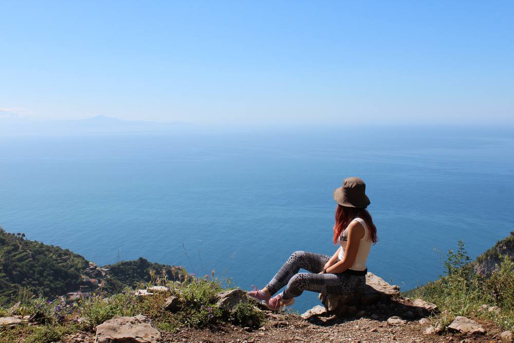 Ragazza escursionista seduta su una roccia che fissa l'orizzonte.