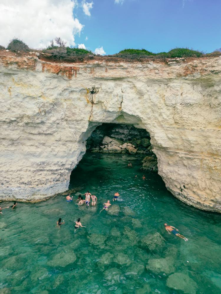 gruppo di giovani che entrano nella grotta della Baia del Mulino d'Acqua in Puglia