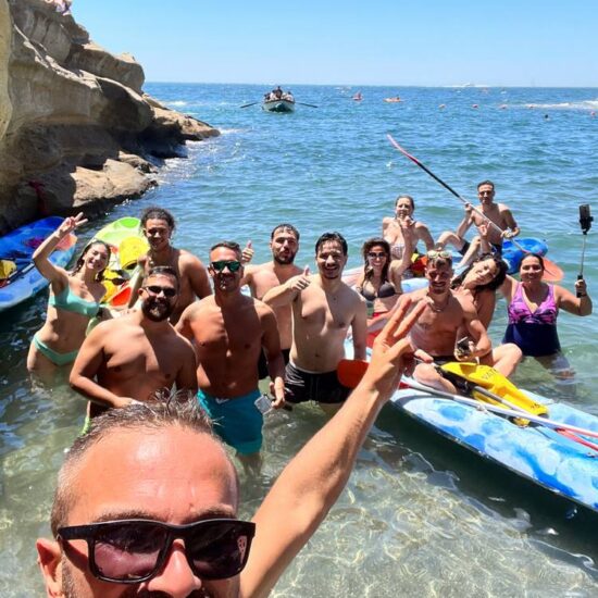 selfie di gruppo di ragazzi che sostano con il kayak nelle acque cristalline di Baia delle Rocce Verdi